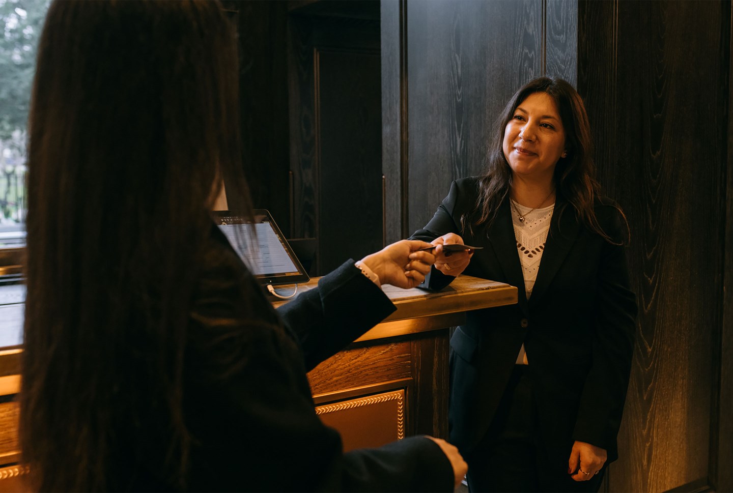 A candid, warm arrival moment inside an IHG property — real colleagues mid-work, guests present, genuine human energy across the brand family.